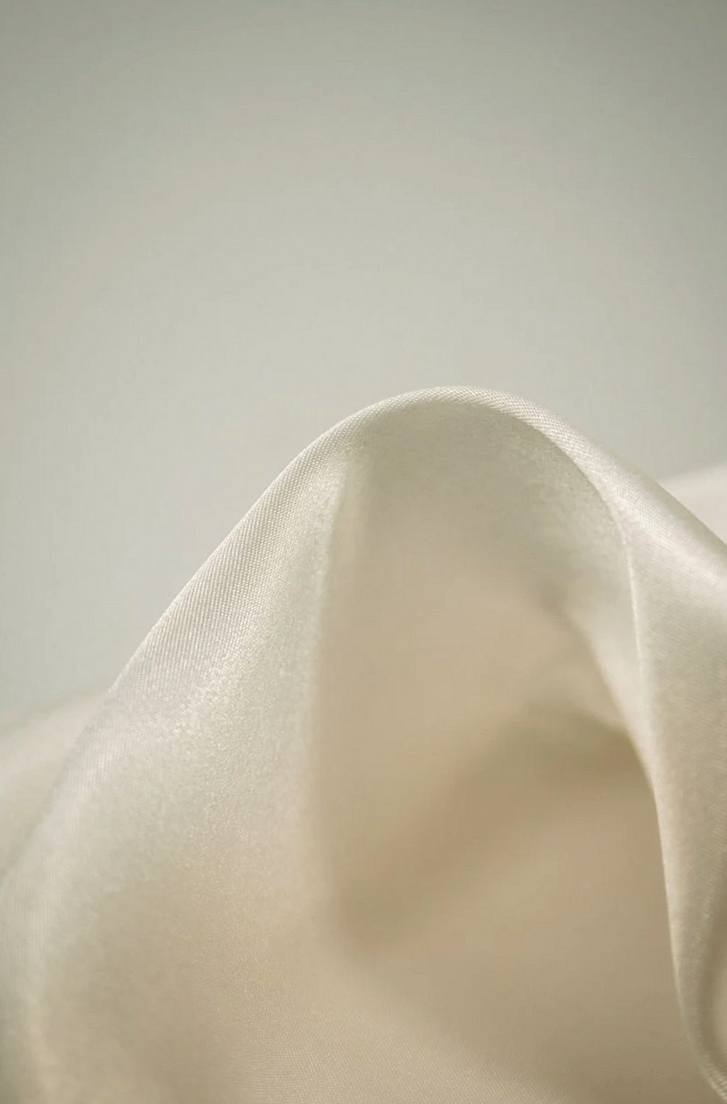 Soft folds of cream silk charmeuse, one of the fabrics used for bodysuits